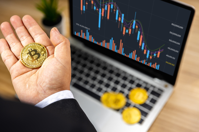 Business bitcoin on hand of investor with graph chart on laptop on wood table