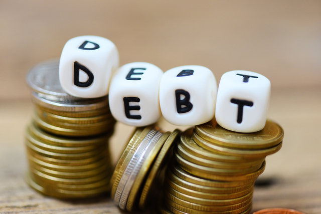 Debt concept with block debt and stacked coins on wooden table background